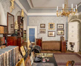 Een bewaard gebleven interieurkamer met boekenplanken, ingelijste portretten aan de muur, een kroonluchter en een houten kast.