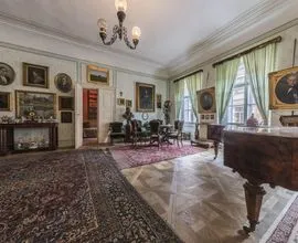 Sfeervolle kamer met antiek meubilair, ingelijste portretten, een kroonluchter en een groot tapijt