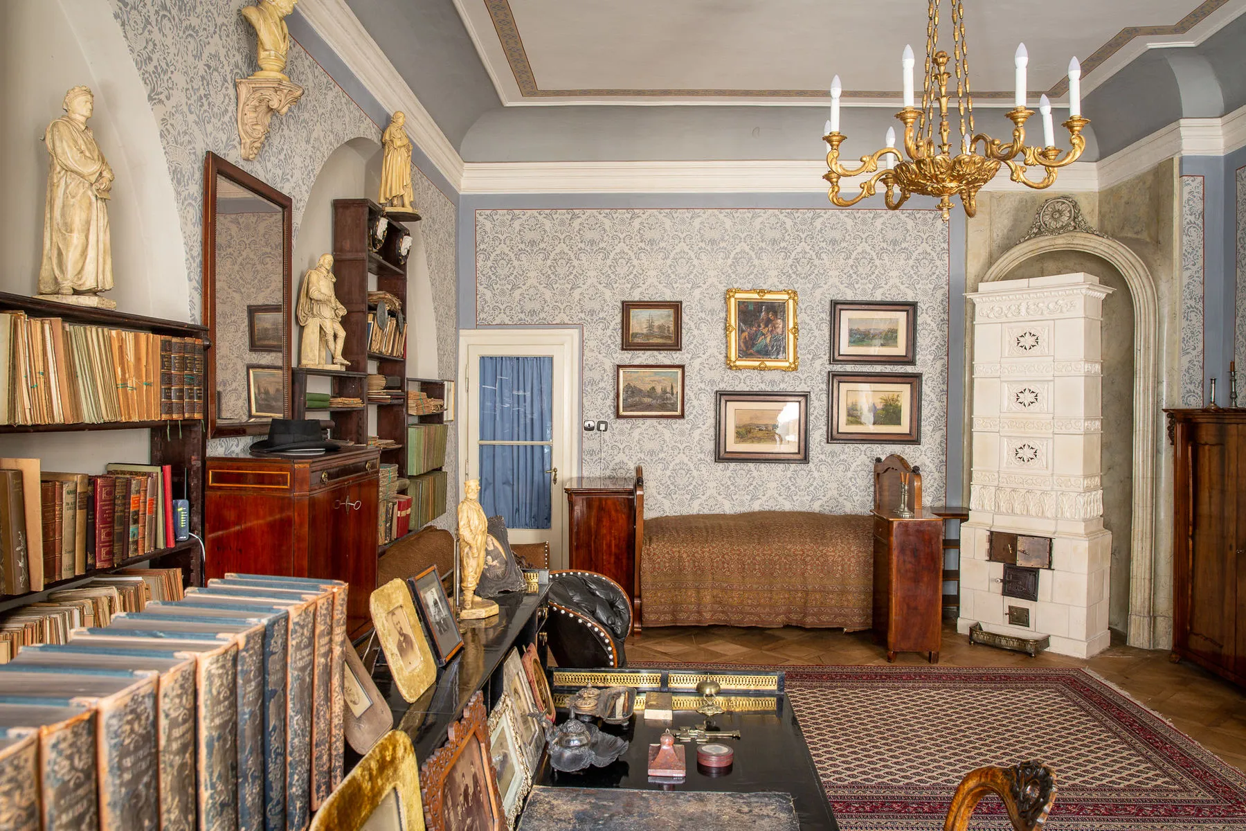 interieur van een historische kamer met boekenplanken, ingelijste foto's, een kroonluchter en een witte kachel