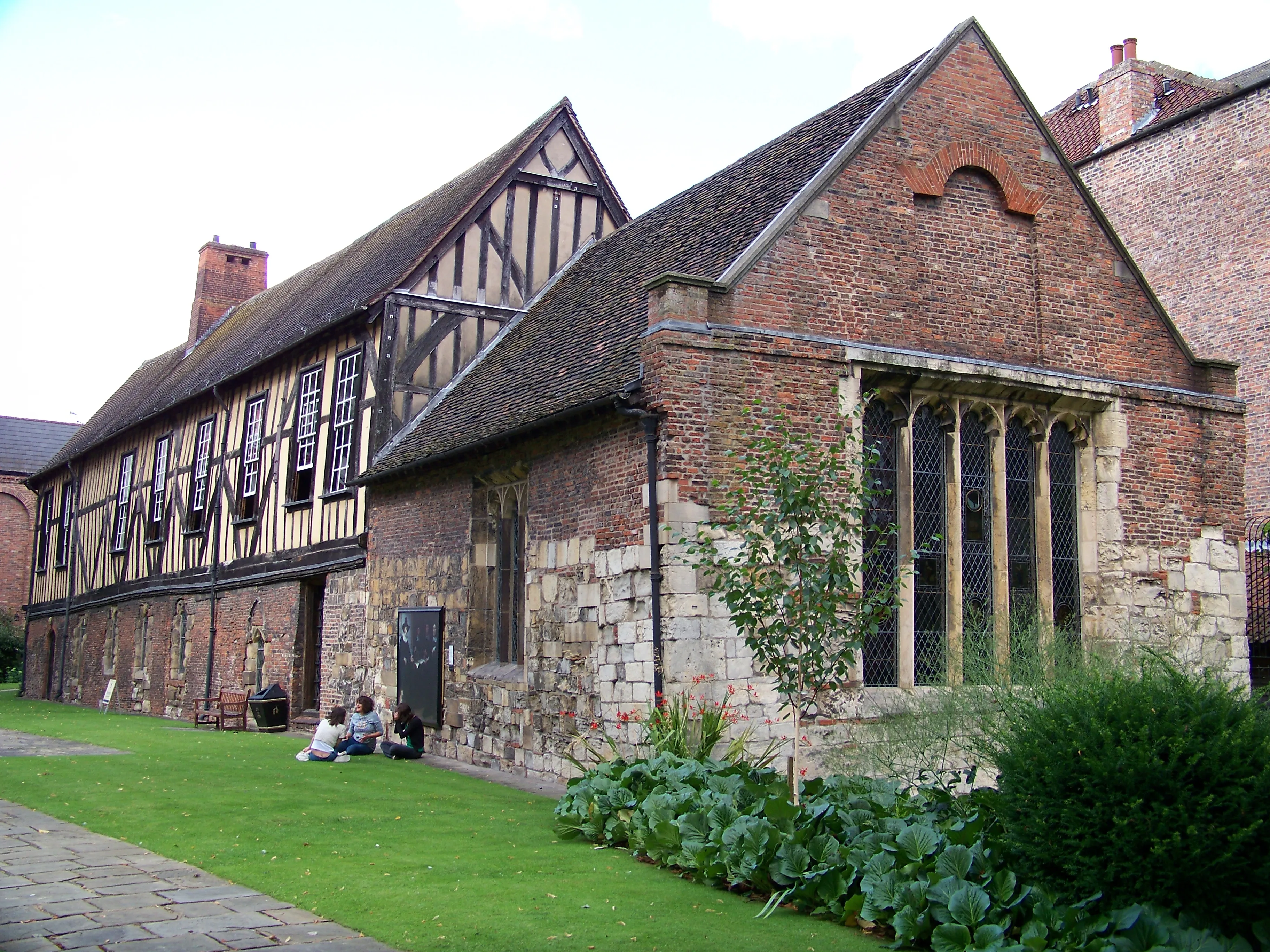 Exterior view of Merchant Adventurers' Hall showing a medieval timber-framed and brick building with a grassy courtyard and large Gothic-style arched window