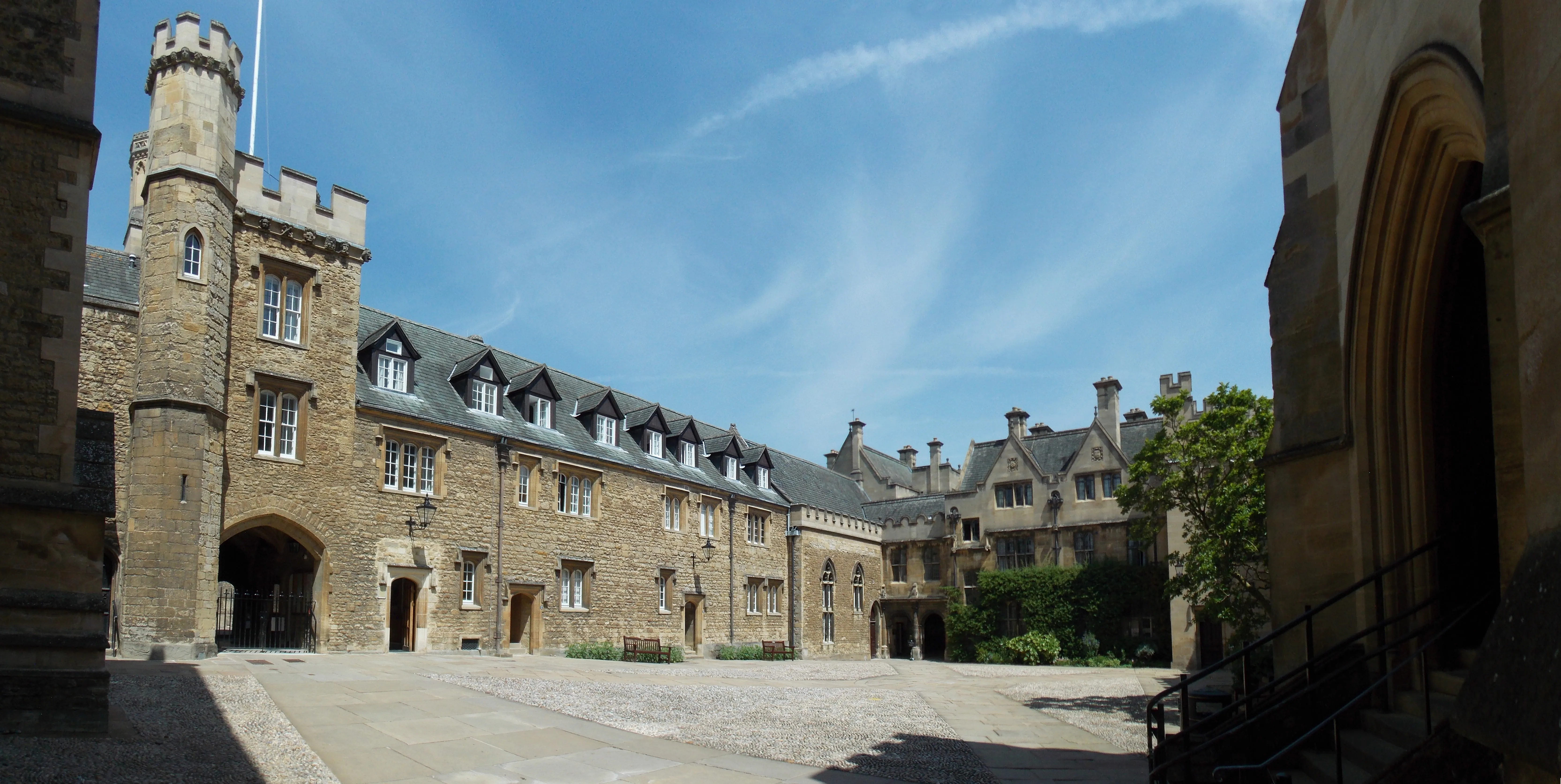 Patio de piedra del Front Quad de Merton College con una torre medieval a la izquierda, una puerta arqueada y edificios históricos bajo un cielo azul