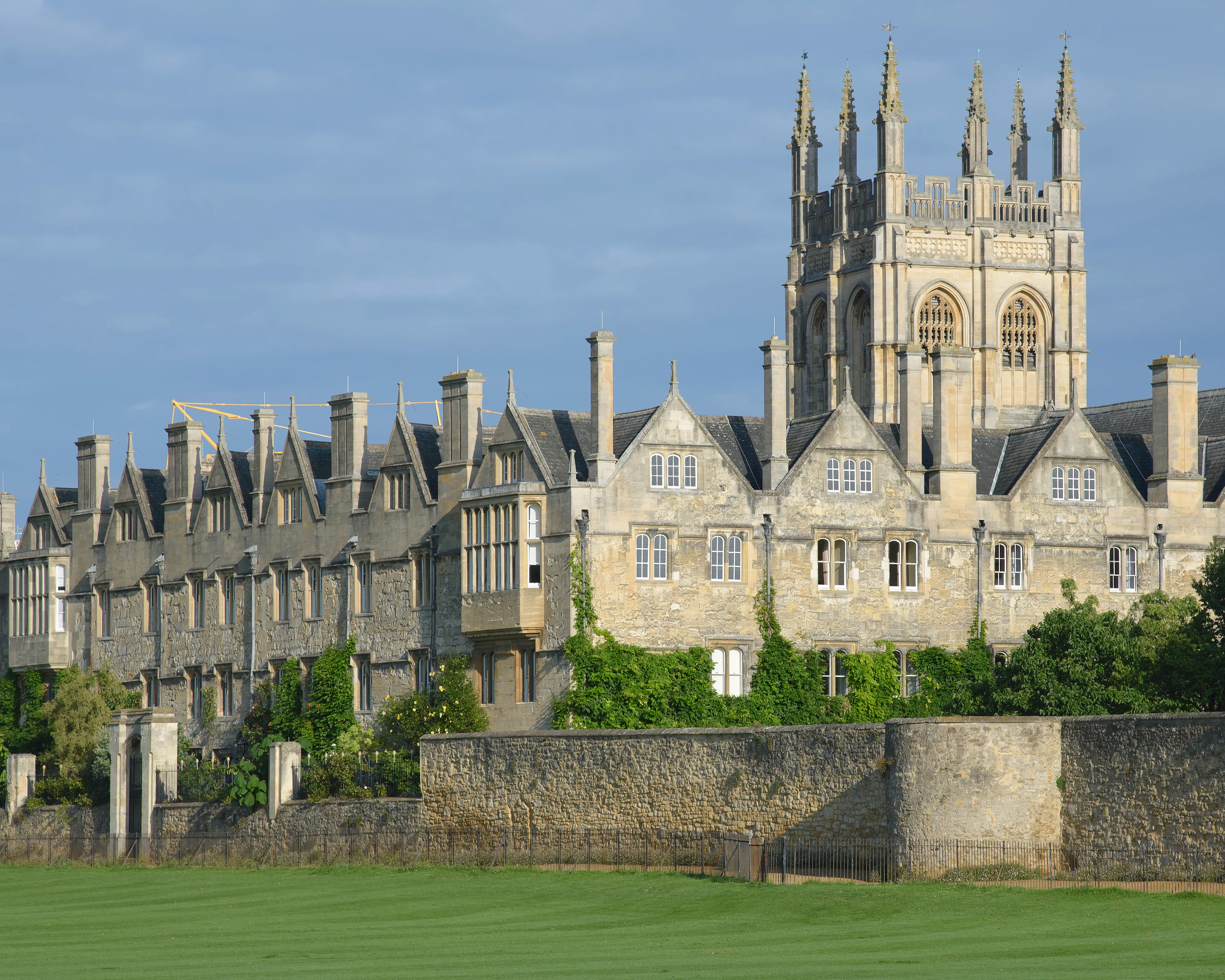 Exterior del Merton College de Oxford mostrando la torre gótica y los históricos edificios de piedra detrás de un césped verde bajo un cielo azul
