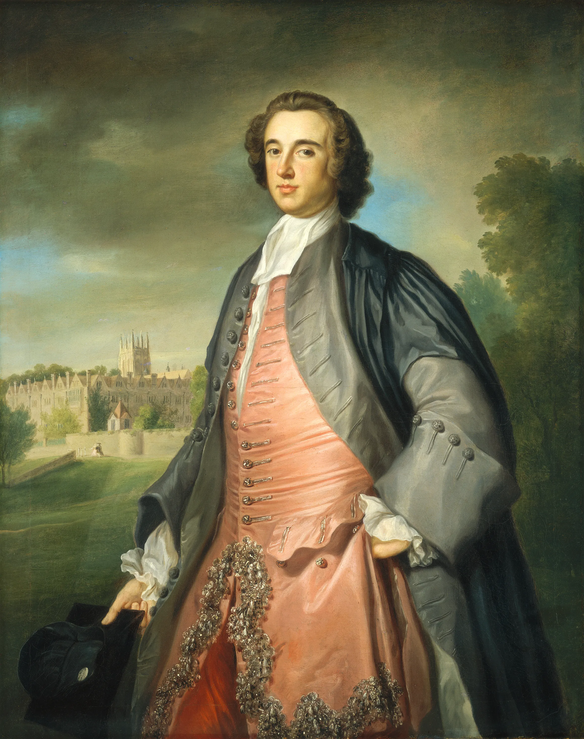 Retrato de cuerpo entero de un hombre con vestimenta académica del siglo XVIII, que incluye una casaca rosa y una toga gris, sosteniendo un birrete negro, con una vista de los edificios universitarios de Oxford al fondo.