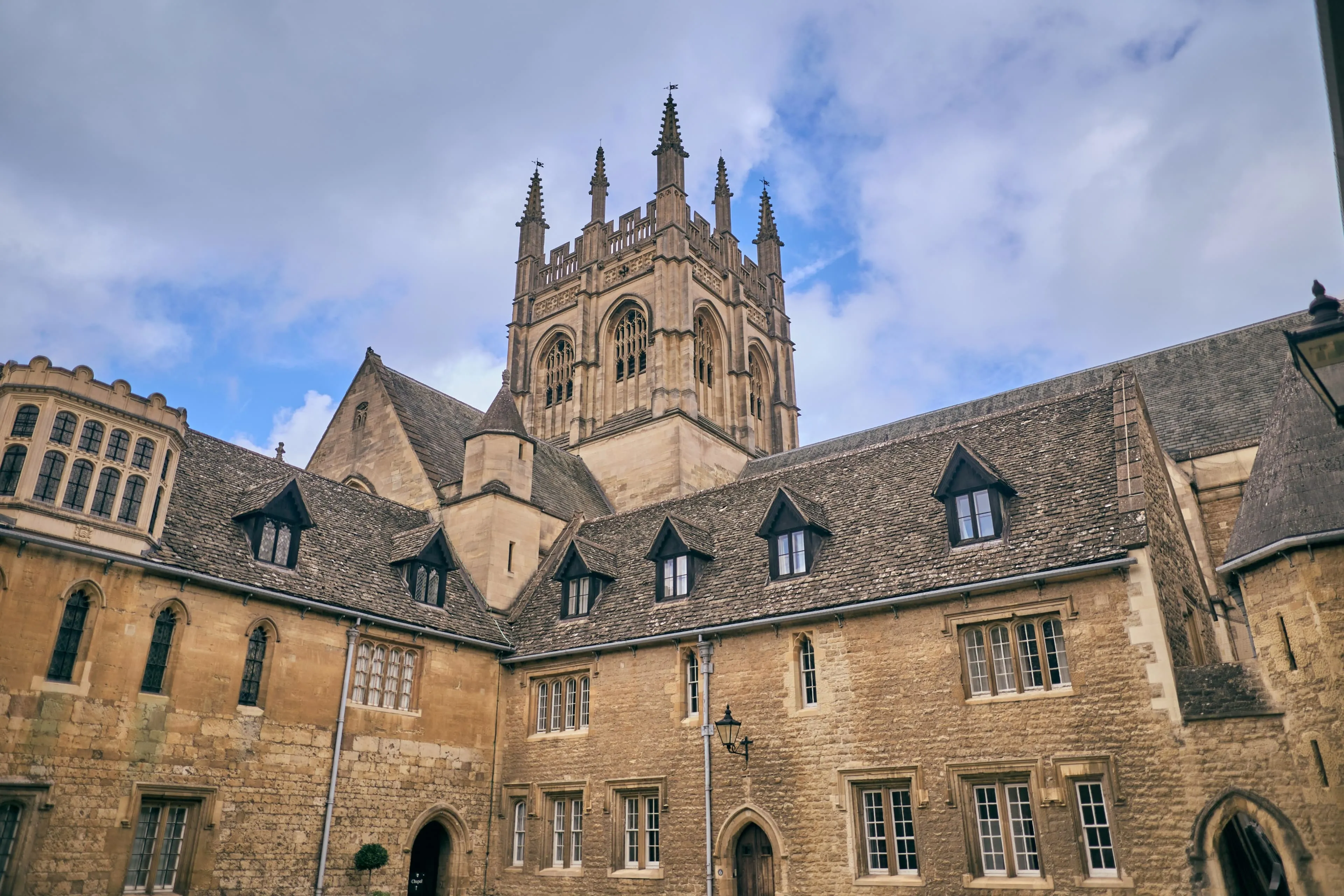Patio de piedra del Merton College con una torre gótica que se alza sobre edificios históricos bajo un cielo nublado