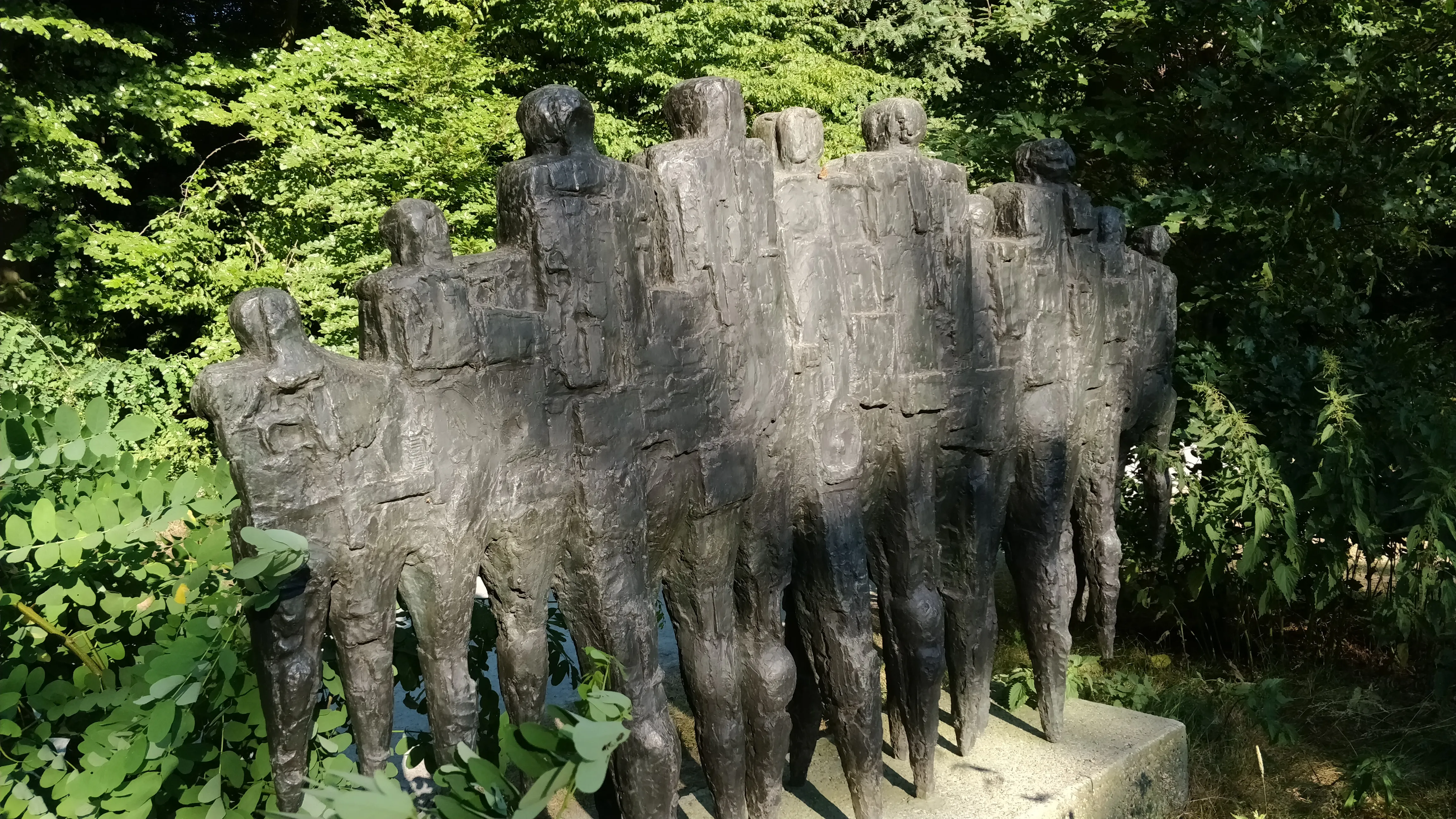 Un grupo de figuras de bronce agrupadas, vistas desde atrás, en un entorno de parque al aire libre.