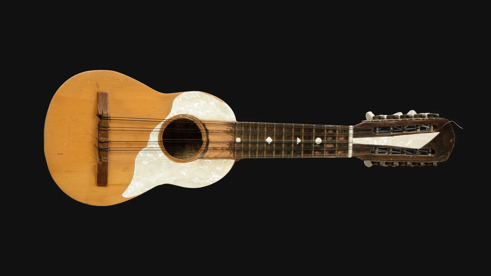 Una guitarra acústica de madera con golpeador blanco, diapasón oscuro con incrustaciones de puntos y clavijero ornamentado, fotografiada sobre un fondo negro