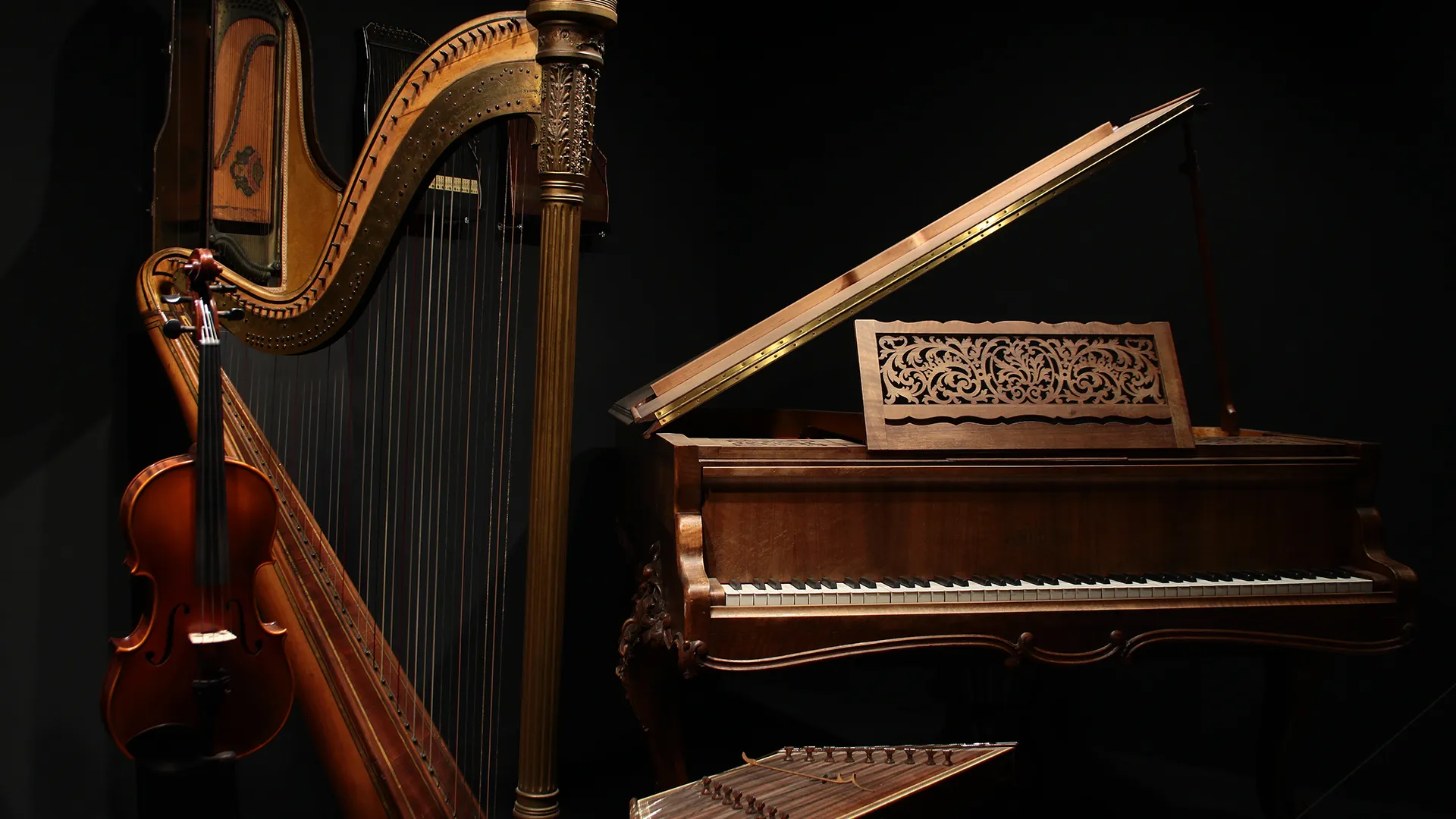 Un arpa, un violín y un piano de cola con una tapa ornamentada expuestos sobre un fondo oscuro.