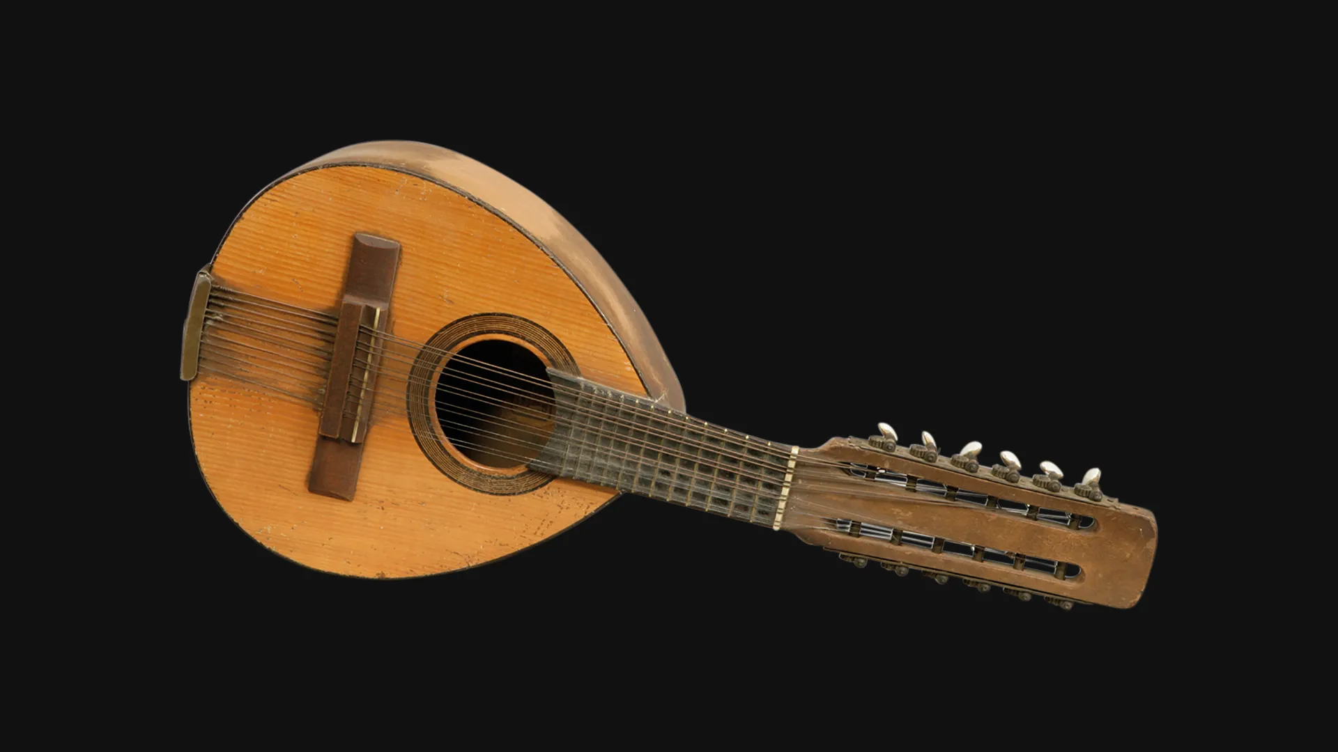Un instrumento de cuerda histórico de madera con cuerpo redondeado, boca, múltiples cuerdas y clavijas ornamentadas, expuesto sobre un fondo negro.