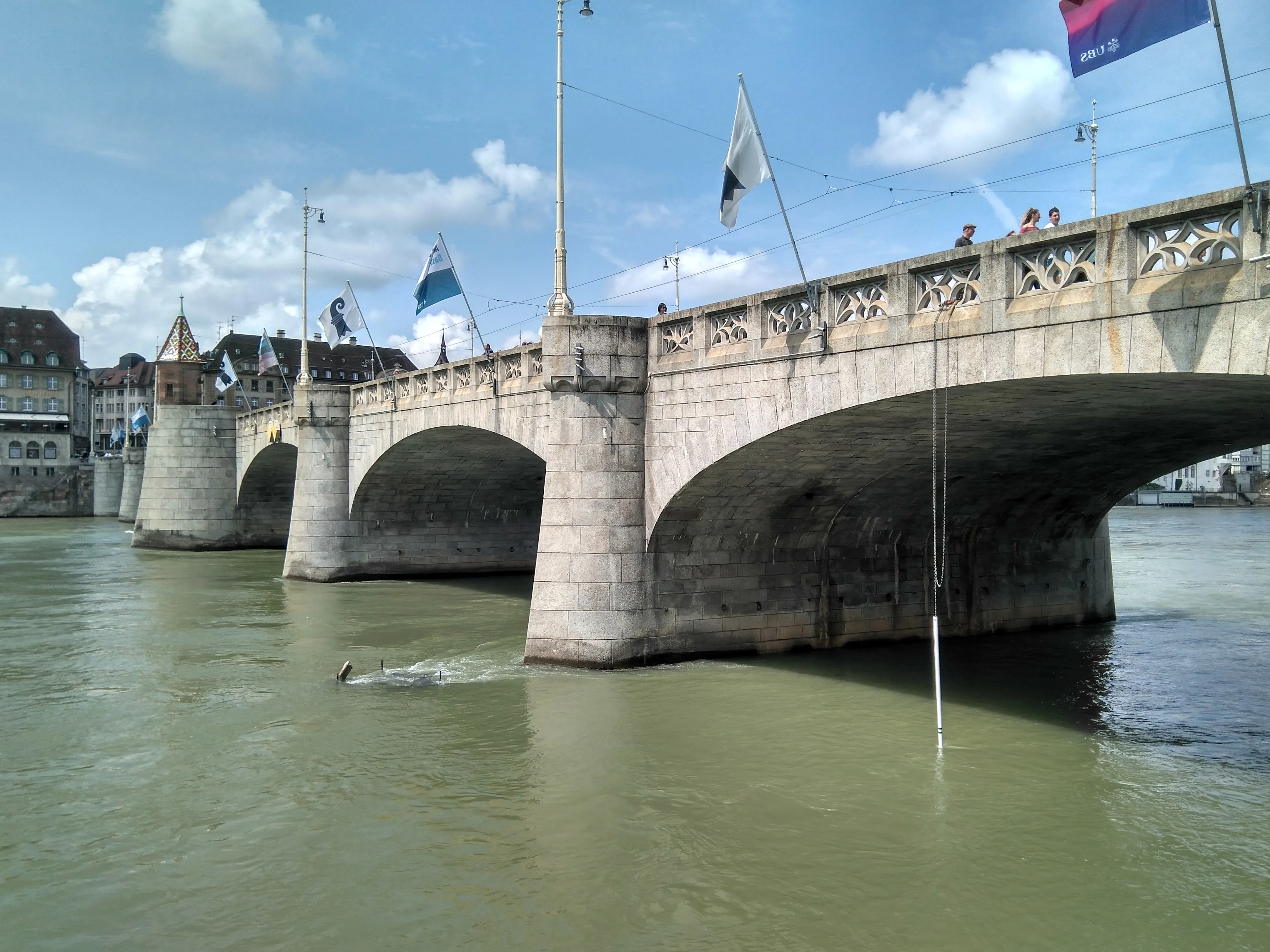 Stenen boogbrug over de Rijn met vlaggen aan masten langs de borstwering, de Mittlere Brücke in Bazel.