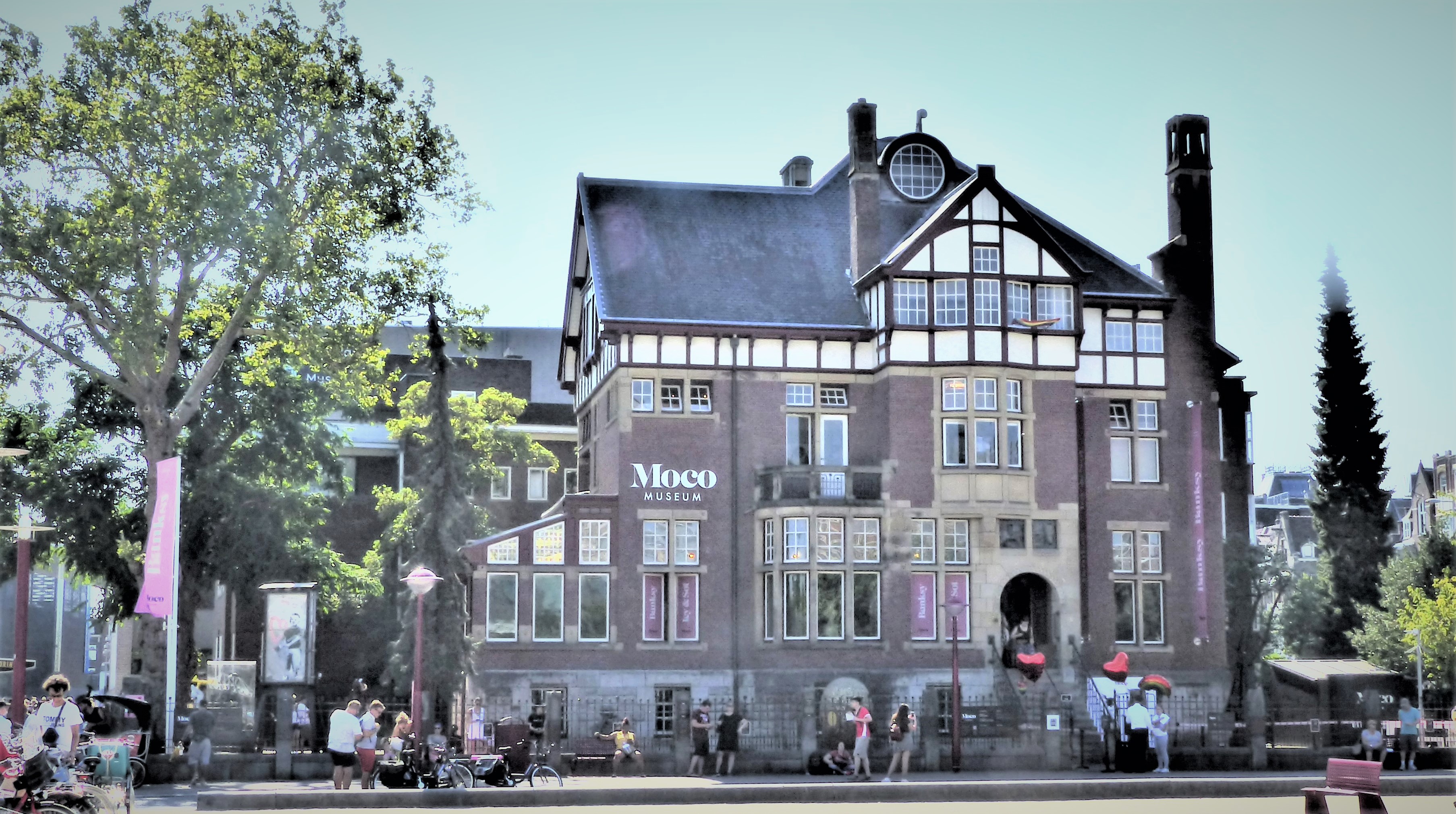 El histórico edificio de ladrillo del Moco Museum con arquitectura de estilo Tudor, con el nombre del museo sobre grandes ventanales, rodeado de árboles y visitantes