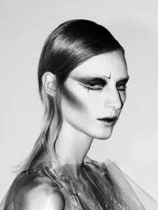 Retrato en blanco y negro de un modelo con un maquillaje de ojos vanguardista y dramático y una prenda metálica