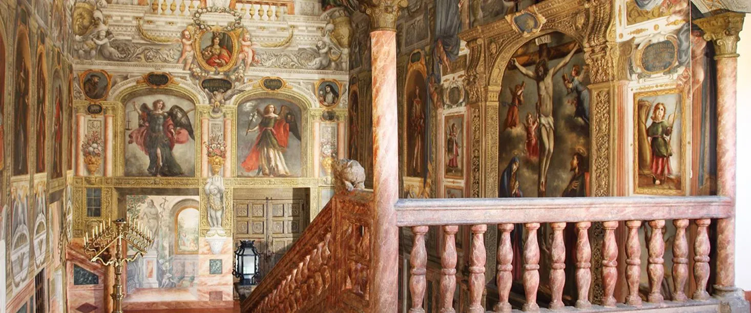 Ornate interior of Monasterio de las Descalzas Reales with religious paintings, frescoes, and a wooden staircase
