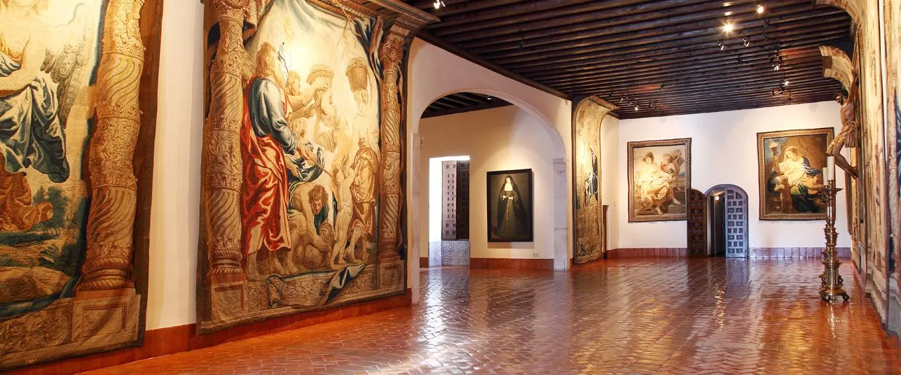 Interior hallway with large tapestries and paintings on the walls, wooden floor, and arched doorways