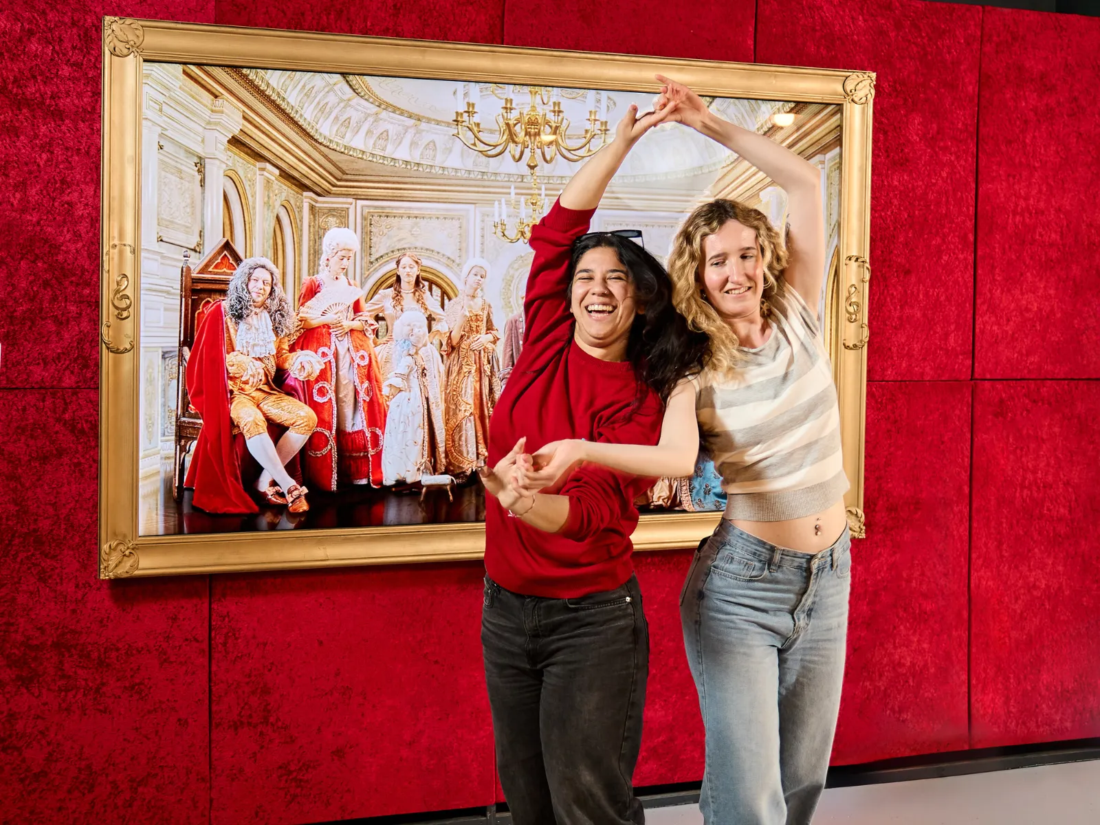 Dos personas posando frente a una pintura enmarcada de figuras históricas en un entorno de museo