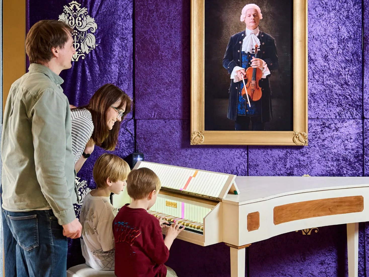 Una familia de cuatro personas interactuando con una exhibición musical en una sala con paredes moradas y un retrato enmarcado de Mozart.