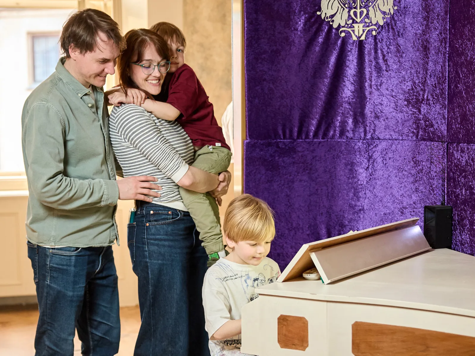 Una familia con dos niños en una exposición de museo con una pared morada y una consola de piano