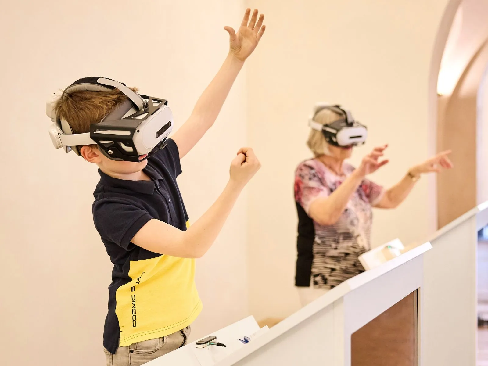 Un niño y una mujer con cascos de realidad virtual, levantando los brazos mientras interactúan con una exhibición.