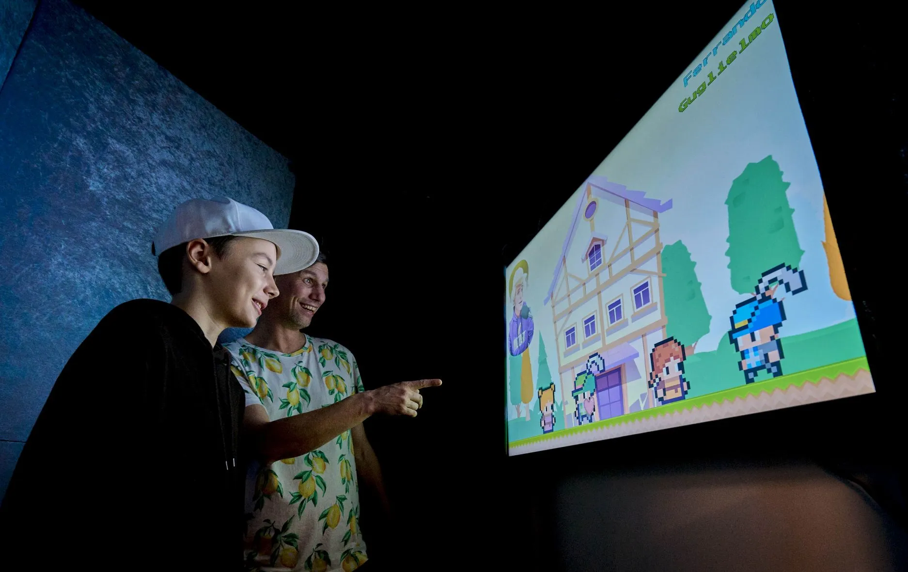Dos personas mirando una pantalla que muestra una colorida escena animada con una casa y personajes de dibujos animados