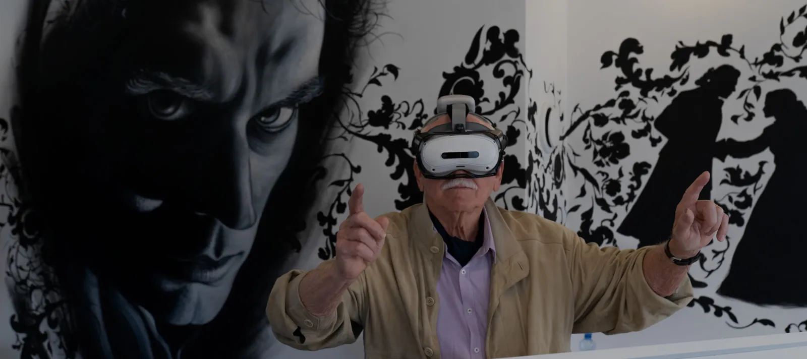 Een man met een VR-headset op, handen in de lucht, staand voor een grote zwart-witte muurschildering van een mannengezicht.