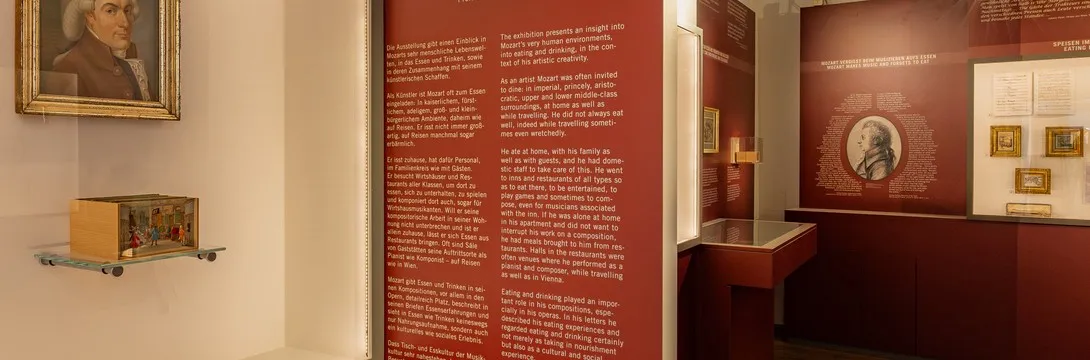 museuminterieur met rode muren, informatieve tekstpanelen en een ingelijst portret van Mozart