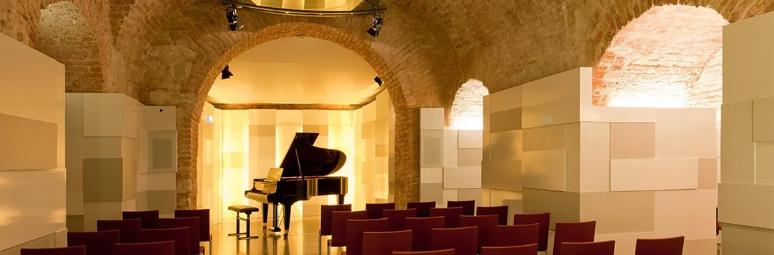 Techo abovedado de ladrillo y un piano de cola en una sala de conciertos con asientos rojos en Mozarthaus Vienna