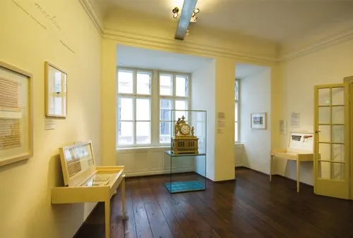 sala de galería de paredes amarillas con suelos de madera, documentos enmarcados y una vitrina de cristal que contiene un reloj