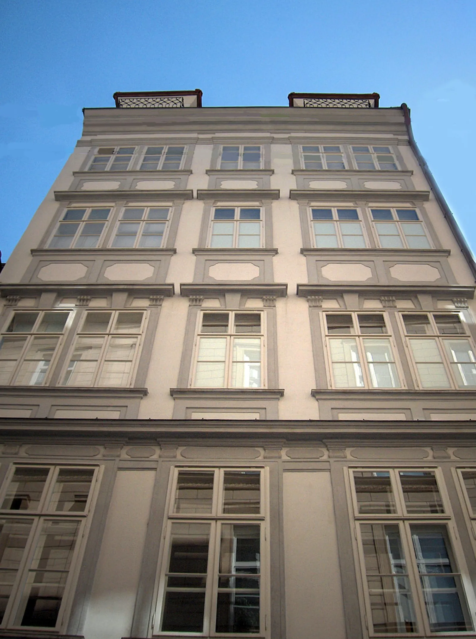 fachada de edificio clásico con múltiples ventanas y trabajos de piedra decorativos bajo un cielo azul