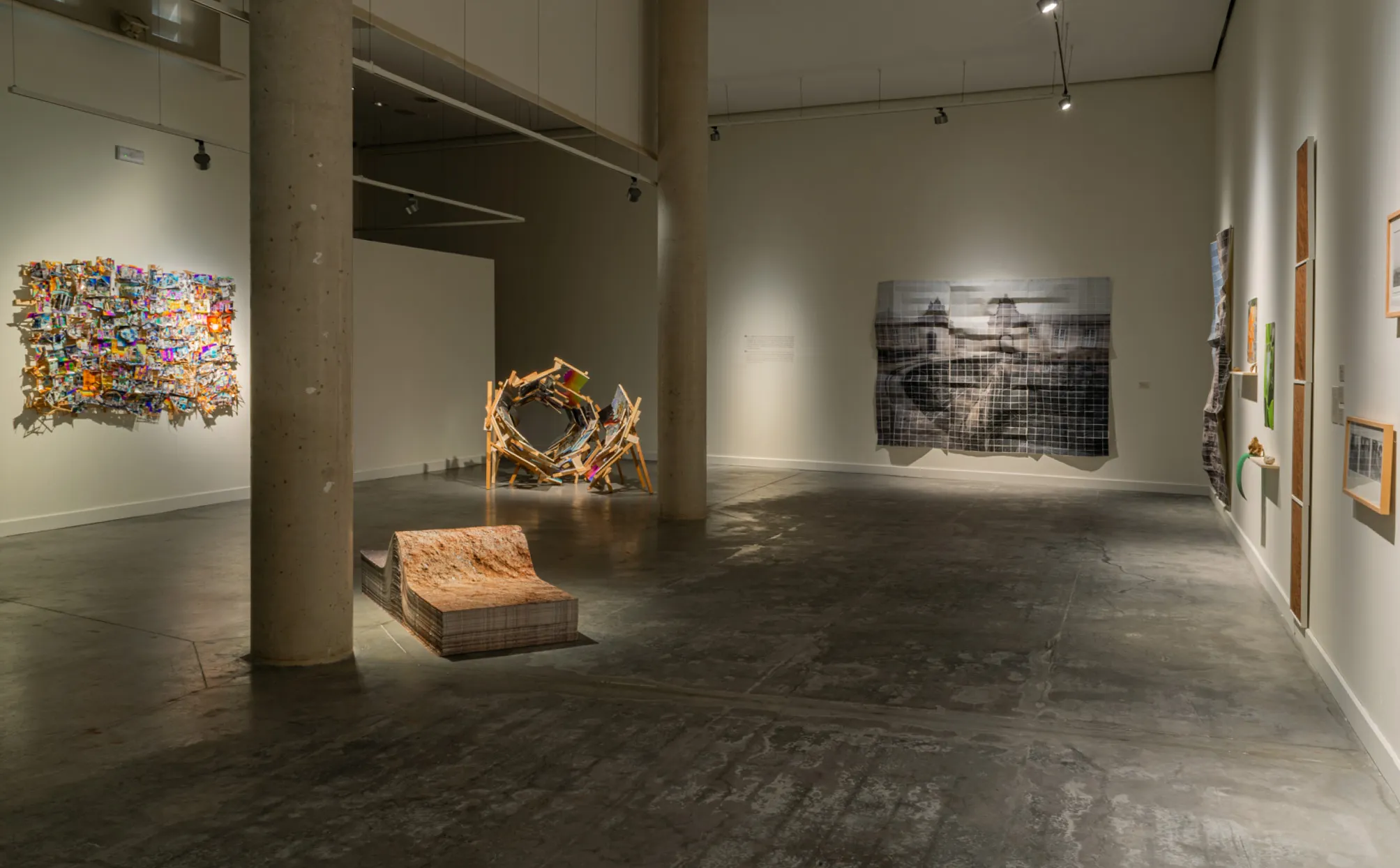Interior de una galería con columnas de hormigón, iluminación de riel y múltiples obras de arte contemporáneo, incluyendo piezas montadas en la pared y esculturas de suelo.