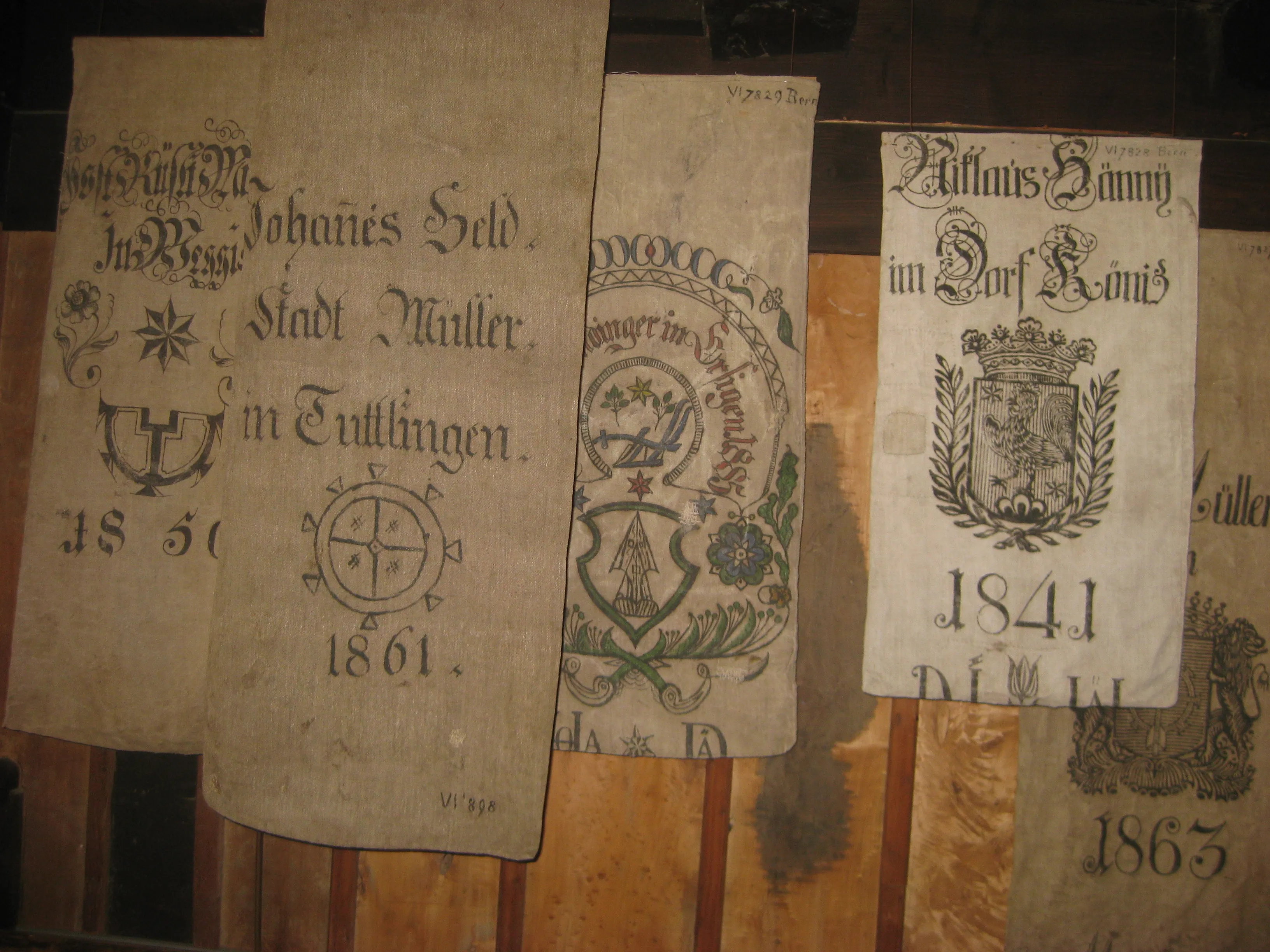 Historyczne worki na mąkę z XIX wieku z nadrukowanymi herbami, datowane na lata 1841–1863, z tekstami w języku niemieckim, wiszące na drewnianej ścianie w Watermill Museum Brüglingen