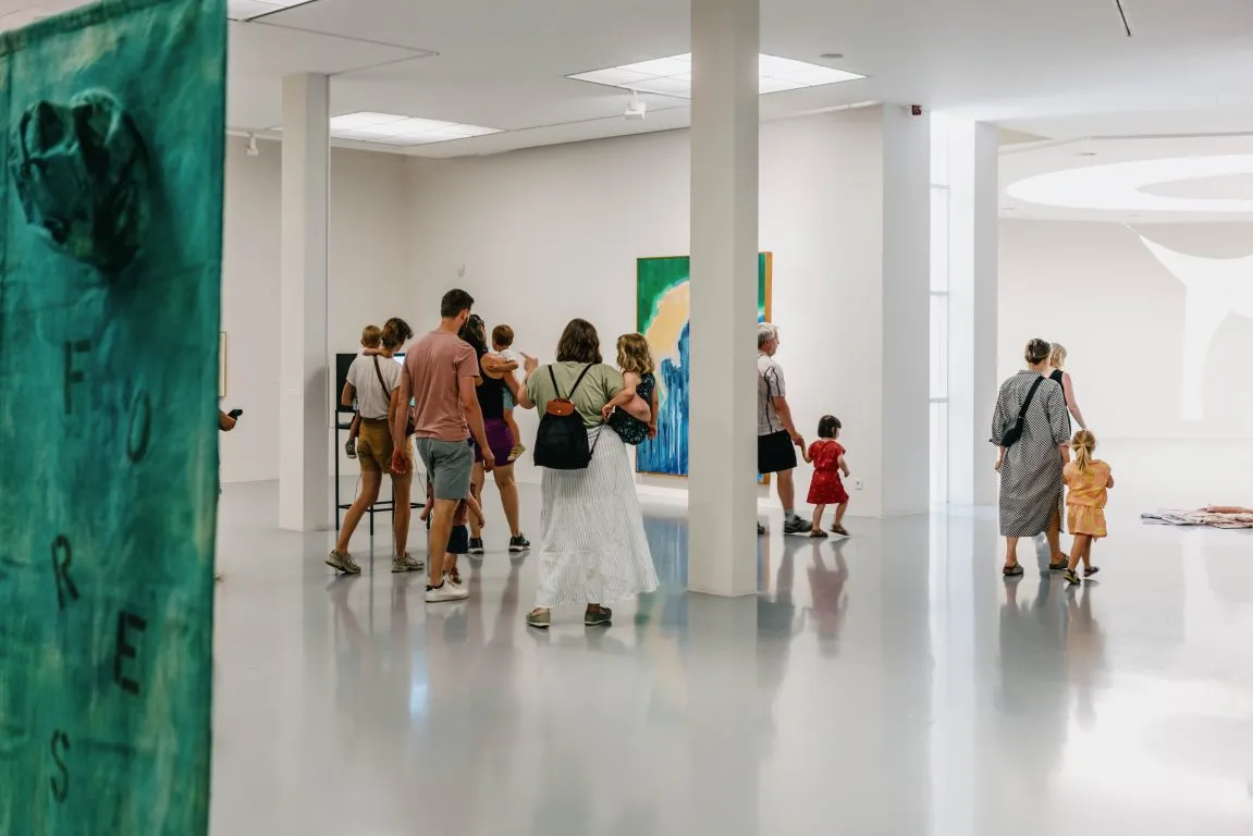 Visitantes explorando una galería de museo luminosa de paredes blancas con grandes pinturas contemporáneas y una obra de arte verde con textura en primer plano.