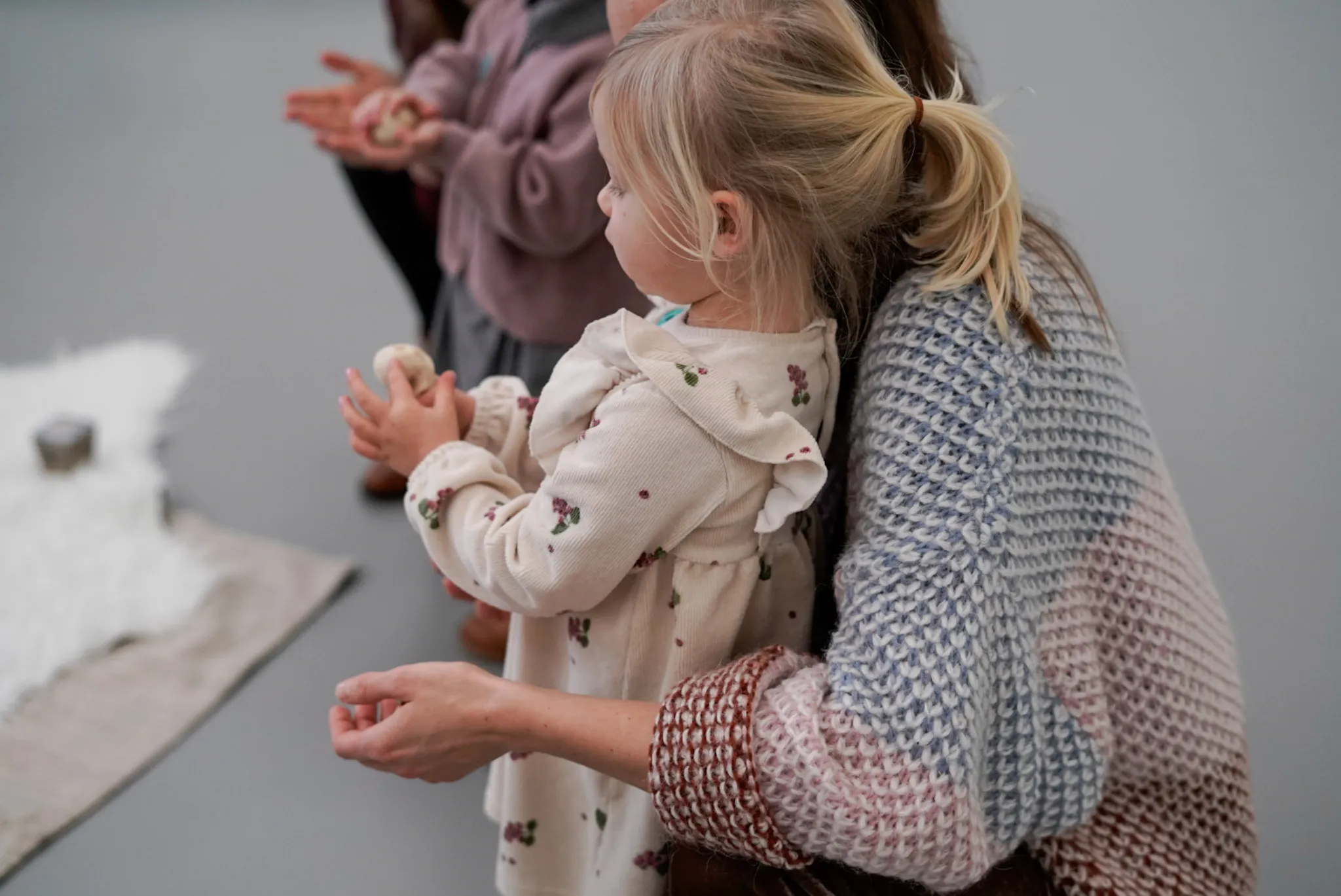 Una niña pequeña con una coleta rubia y un adulto están de pie uno al lado del otro, observando una obra de arte blanca con textura en el suelo de una galería de un museo.