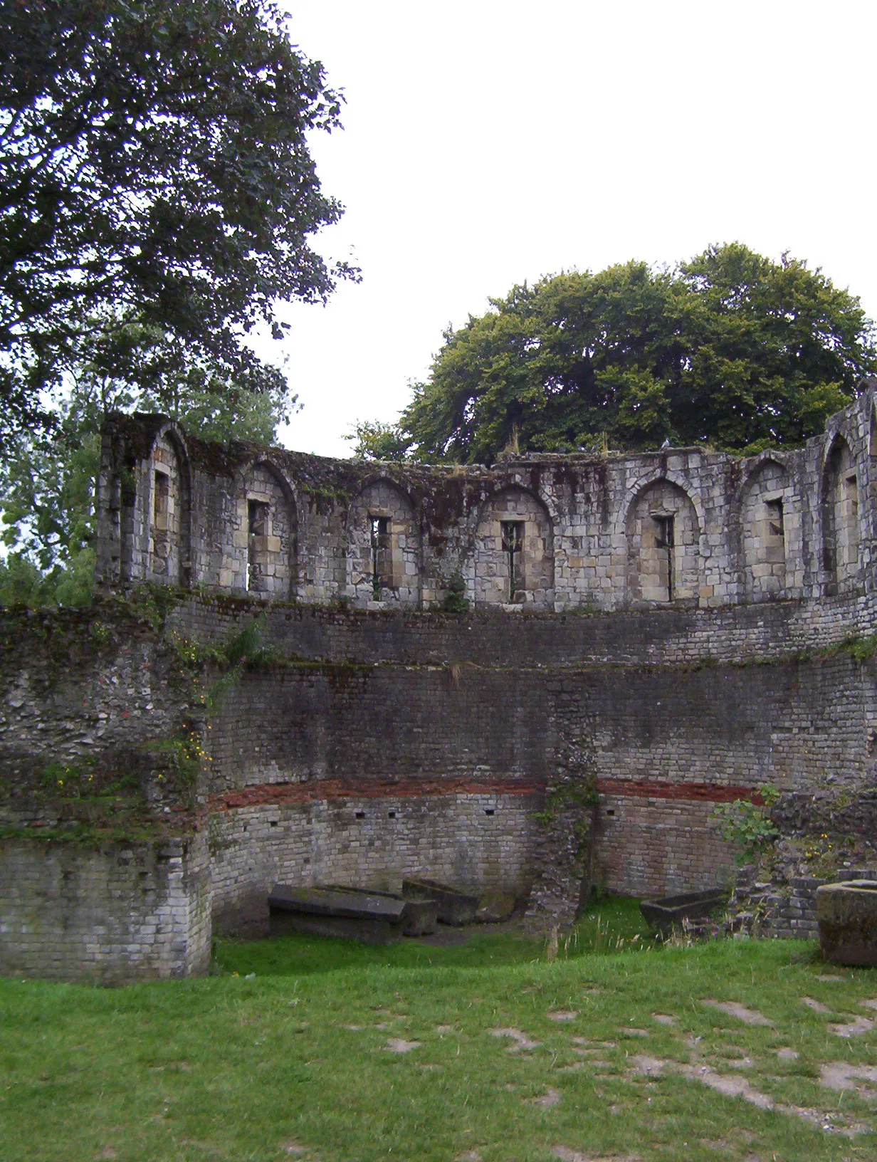 Curved interior stone wall of the Multangular Tower featuring arched niches, a horizontal band of red brick, and wooden benches at the base.