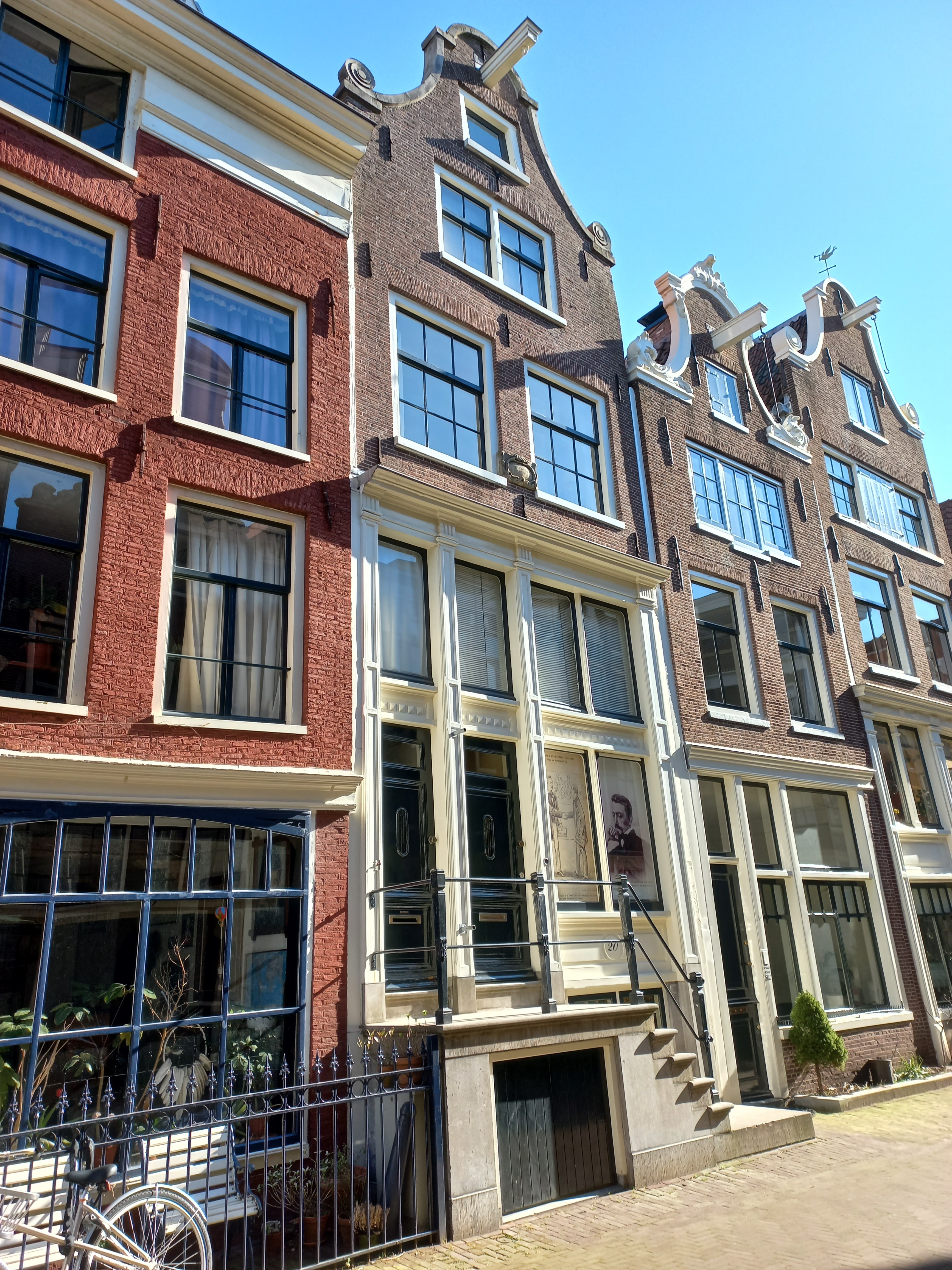 Tradycyjne holenderskie kamienice nad kanałem z fasadami szczytowymi w Amsterdamie, pokazujące budynek Muzeum Multatuli przy Korsjespoortsteeg 20 o charakterystycznej architekturze i dużych oknach
