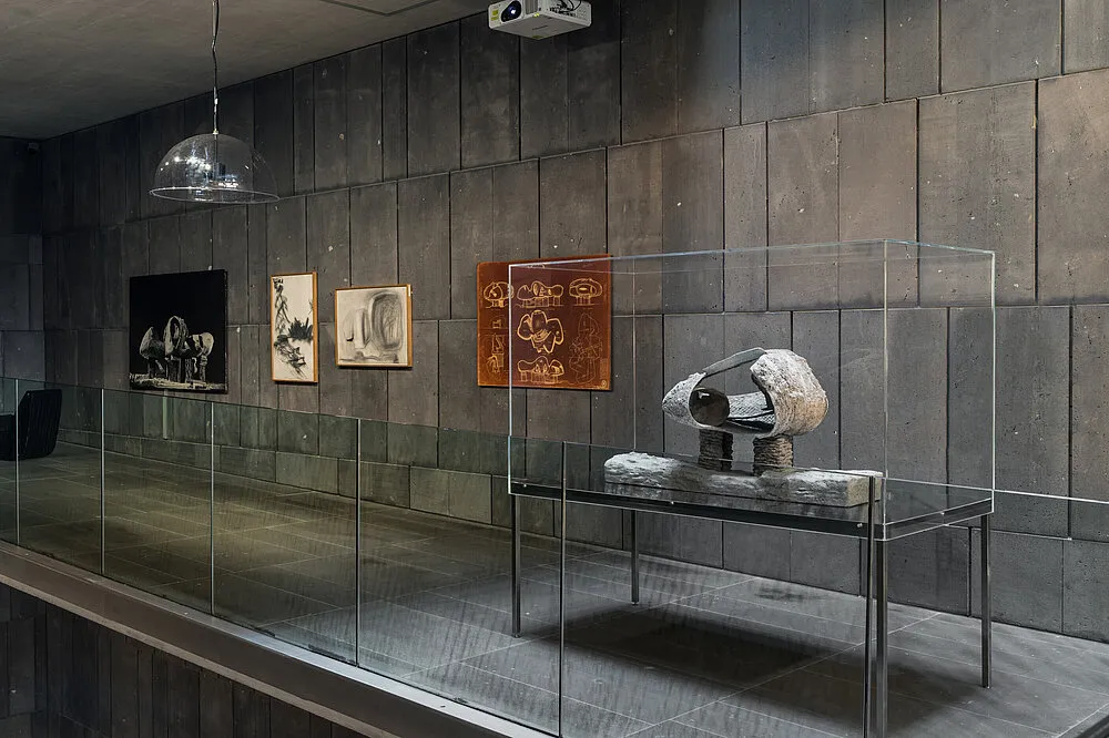 Una escultura en una vitrina con obras de arte enmarcadas sobre una pared oscura en una galería de museo