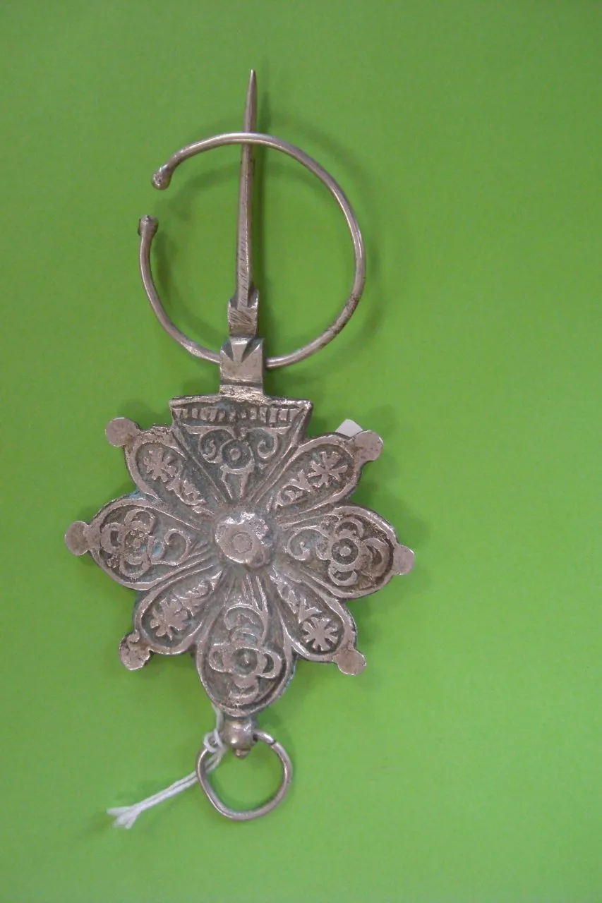 silver brooch with floral design and circular loop on green background