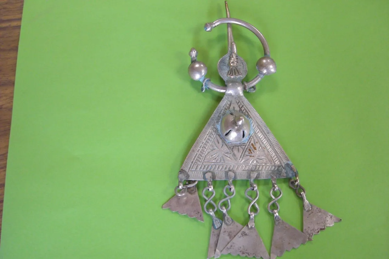 silver pendant with triangular design and dangling elements on green background