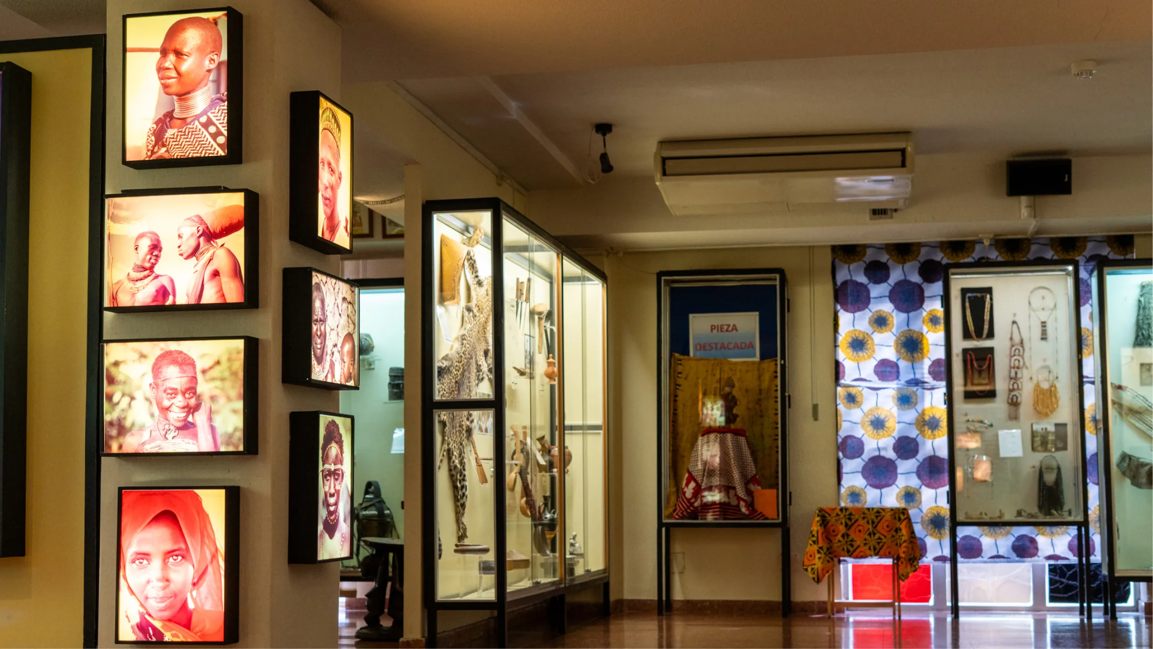 Interieur van een museum met verlichte portretten aan de muur en vitrines met artefacten