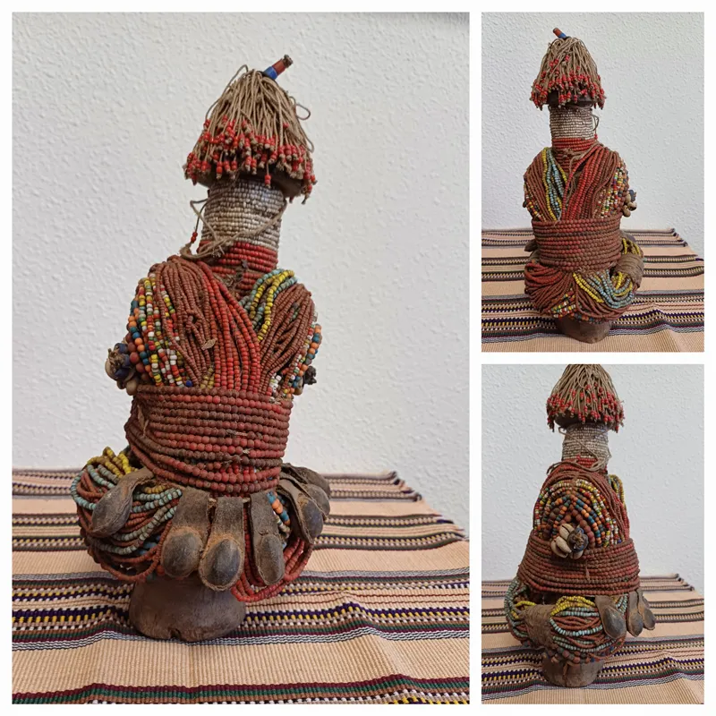 Een traditionele Afrikaanse vruchtbaarheidsbeeldje van hout en kralen, met een hoofdtooisel en lichaam van kralen, zittend op een gestreepte mat.