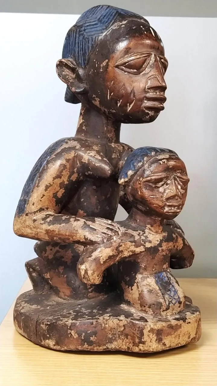 houten sculptuur van een zittende figuur met een kind, met verweerde bruine en blauwe pigmenten