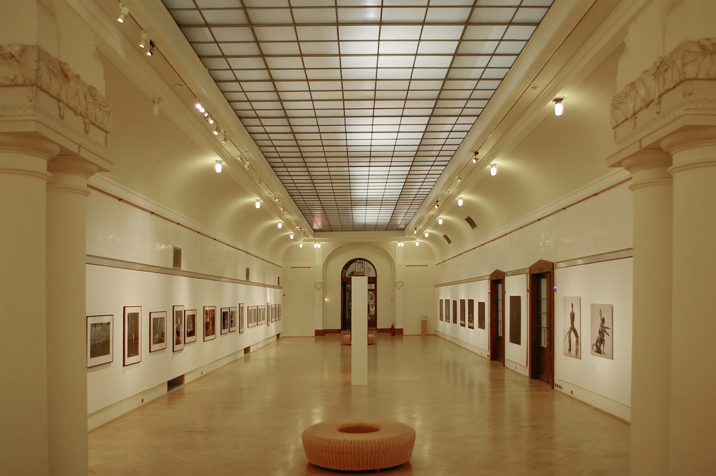 długi hol galerii z wysokim sufitem, oprawione dzieła sztuki na ścianach i okrągła ławka