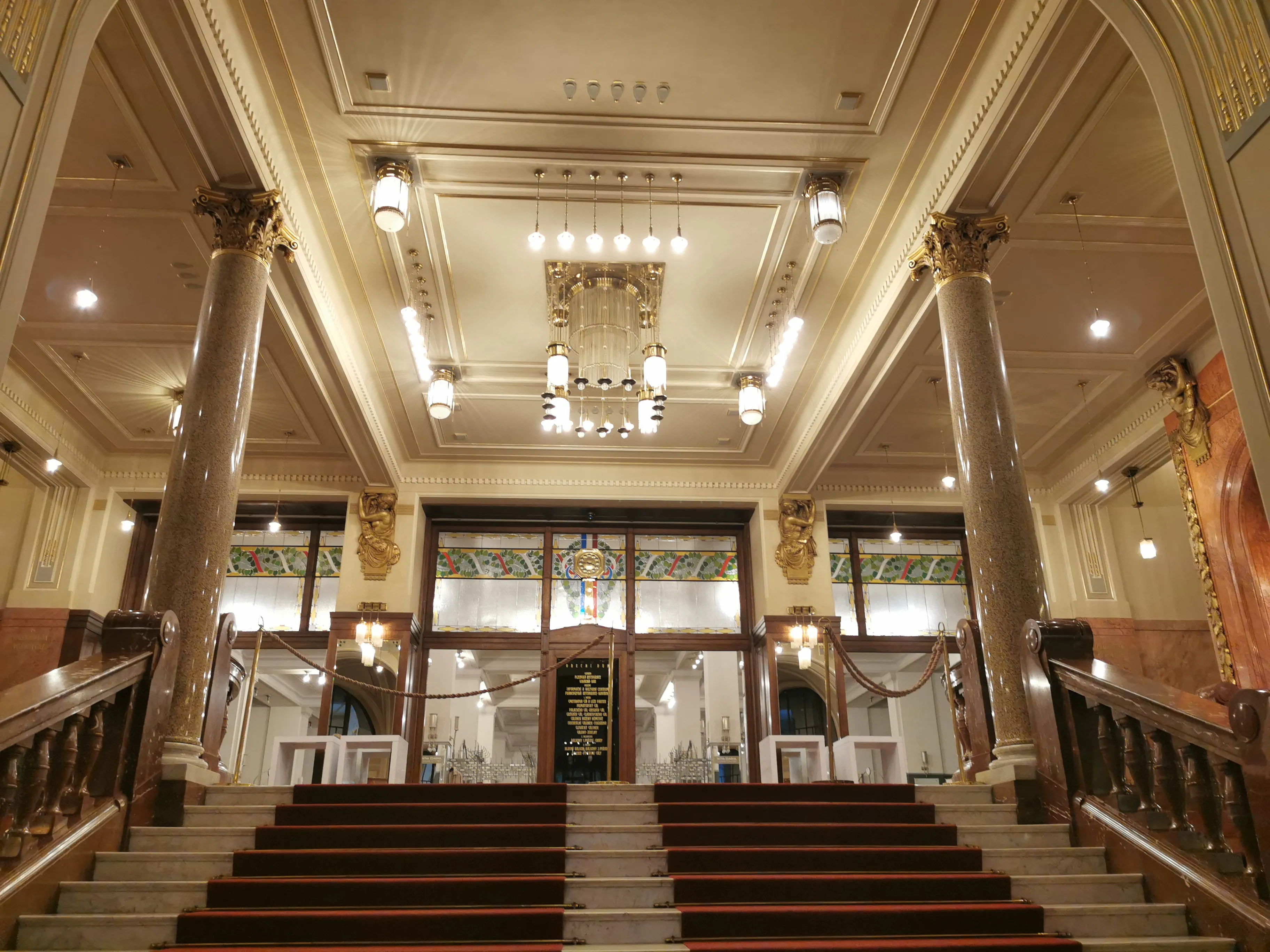 Gran escalera que conduce a un salón ornamentado con columnas de mármol, candelabros y detalles decorativos en el techo