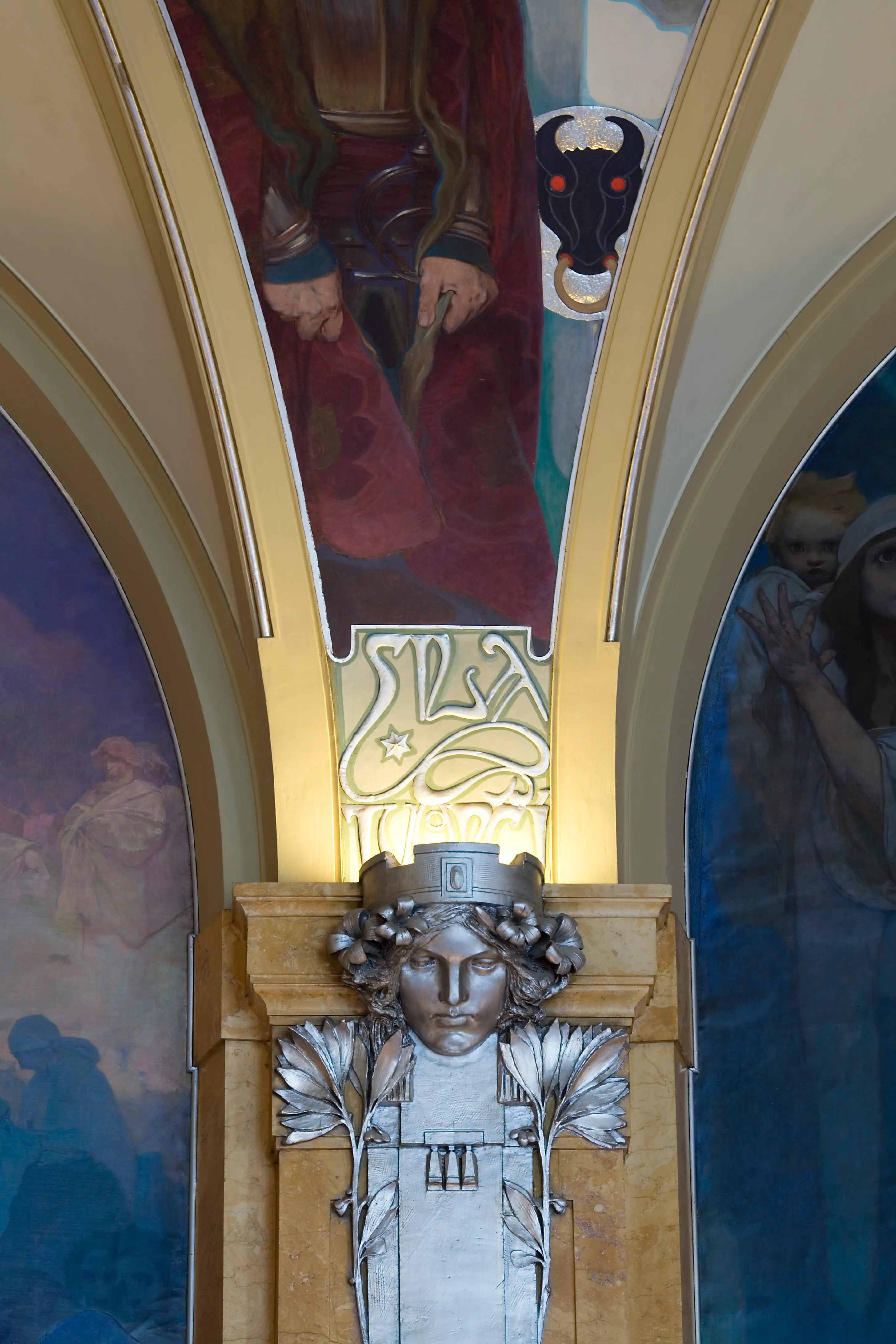 Escultura Art Nouveau de un rostro con elementos florales y un mural pintado al fondo