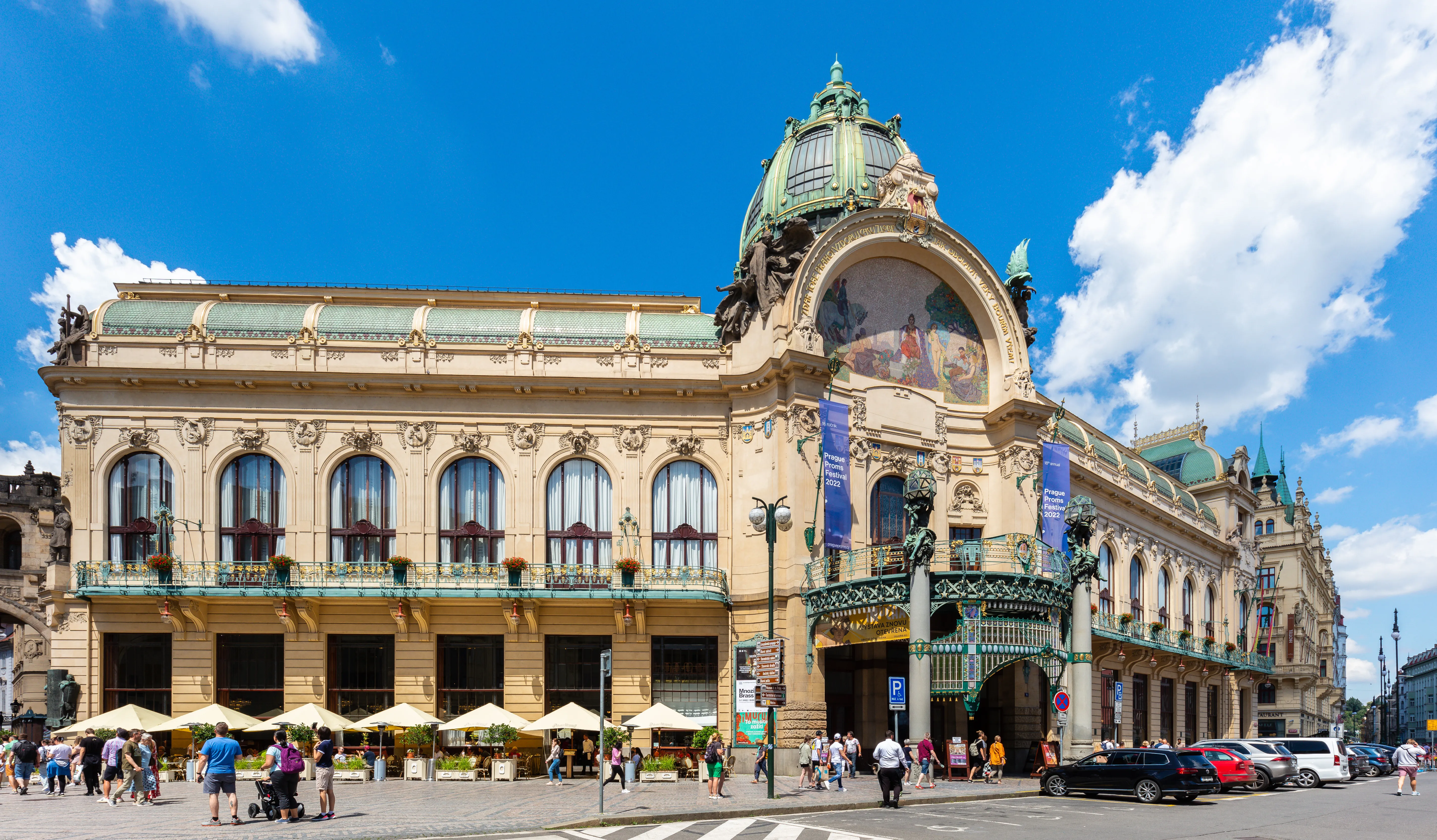 Dom Miejski w Pradze z jego ozdobną architekturą Art Nouveau, zieloną kopułą i łukowymi oknami pod błękitnym niebem z białymi chmurami
