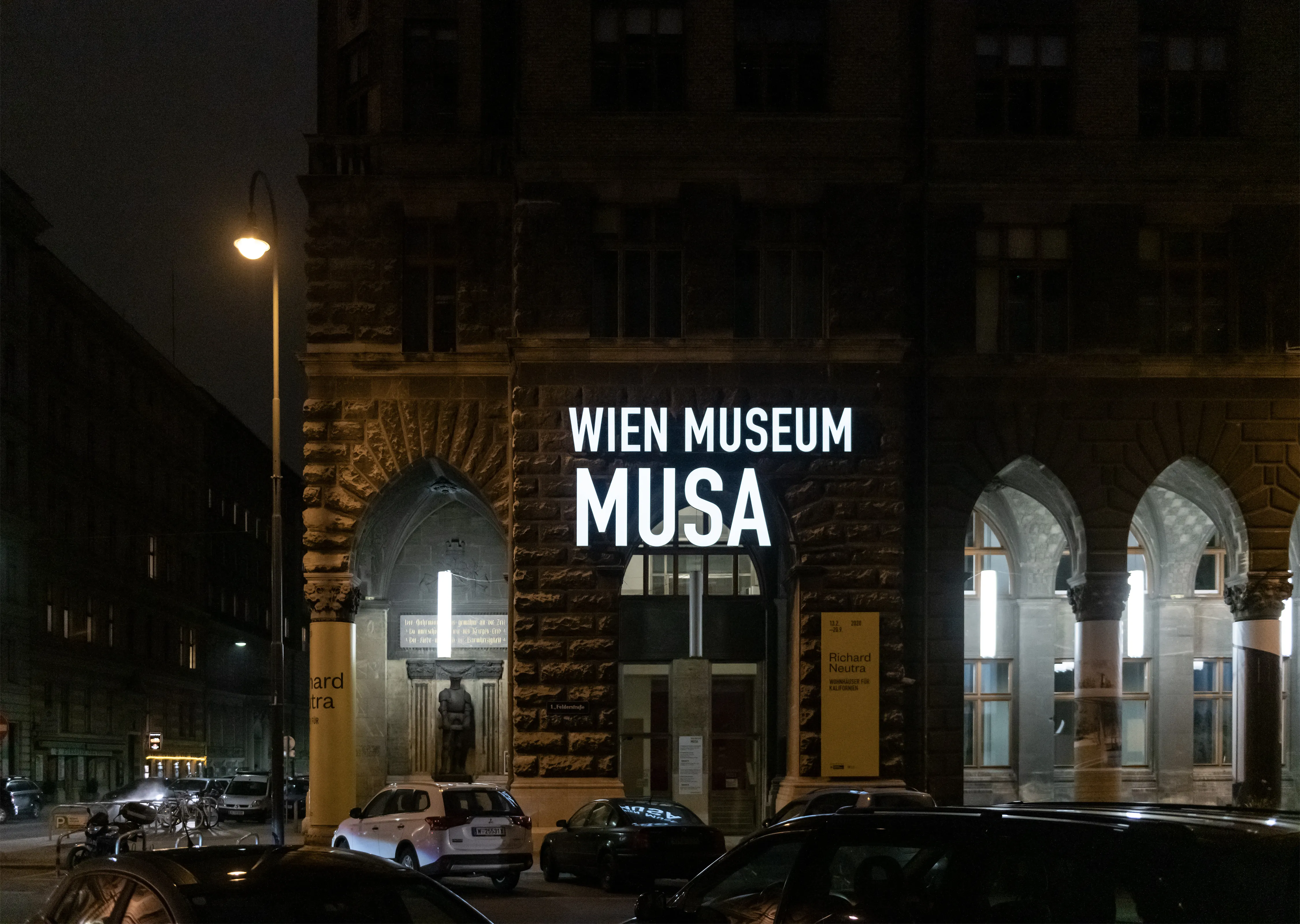 Nachtzicht van het MUSA-gebouw met een verlicht bord met de tekst 'WIEN MUSEUM MUSA' op de gevel