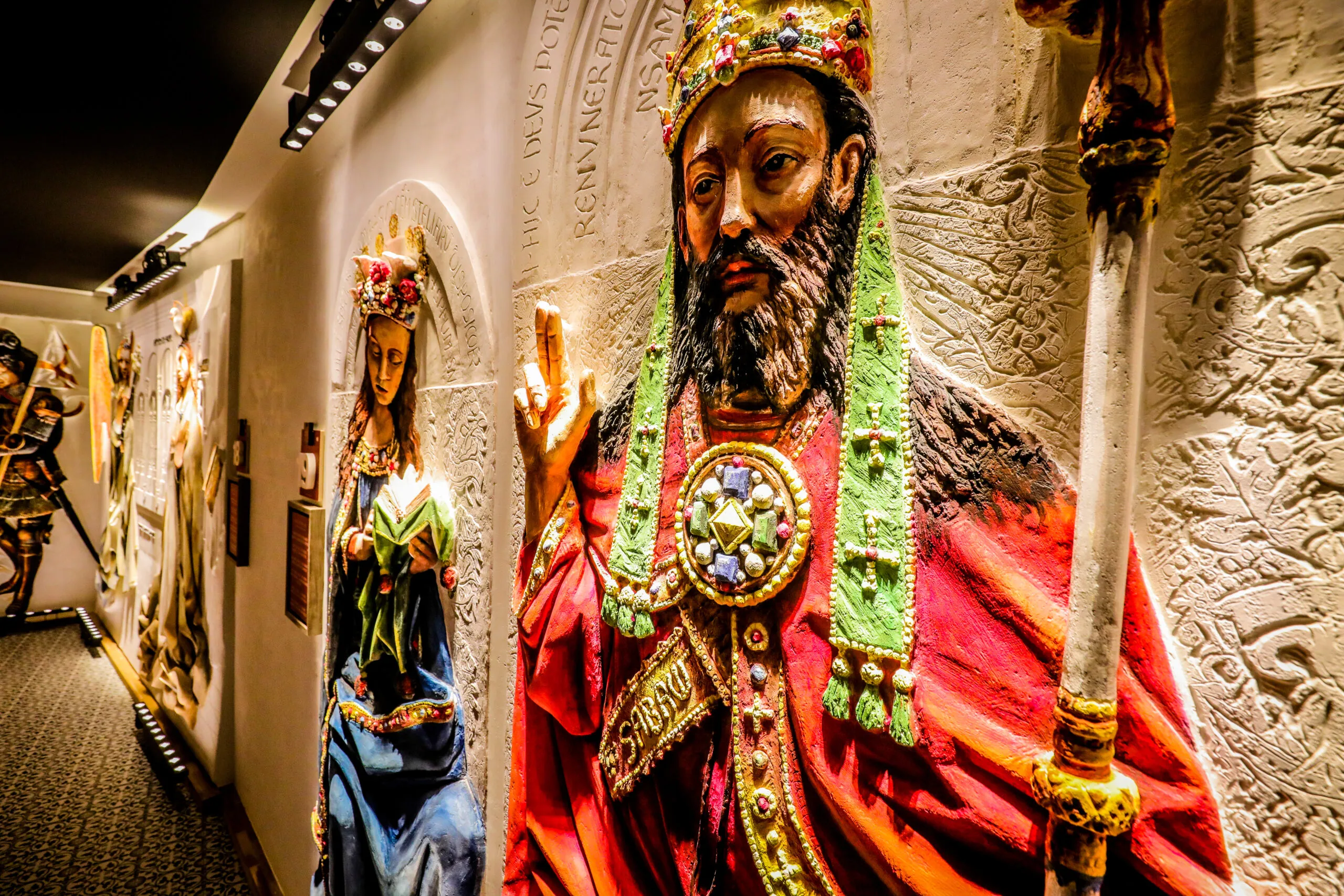 Esculturas en relieve de yeso de gran formato y gran colorido de un rey coronado con un cetro y una reina expuestas en el pasillo de una galería de museo.