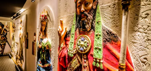 Grandes esculturas en relieve de yeso de colores de un rey y una reina con túnicas, exhibidas en una galería de museo cálidamente iluminada con paredes texturizadas
