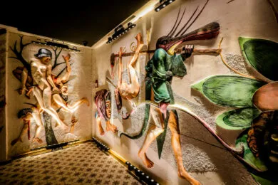 Paredes de galería de museo cubiertas con relieves de yeso a gran escala de figuras y criaturas fantásticas, iluminadas por iluminación de riel sobre un suelo de baldosas estampadas