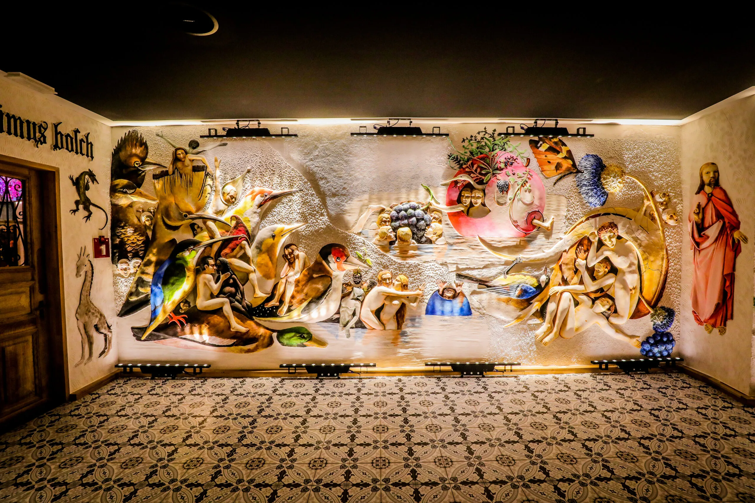 Gran relieve de yeso que cubre una pared del museo, representando múltiples figuras en una composición compleja con iluminación puntual dramática y un suelo de baldosas con patrones debajo.