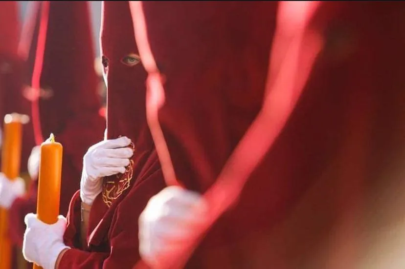 Primer plano de figuras con capirotes y túnicas rojas sosteniendo velas amarillas durante una procesión de Semana Santa