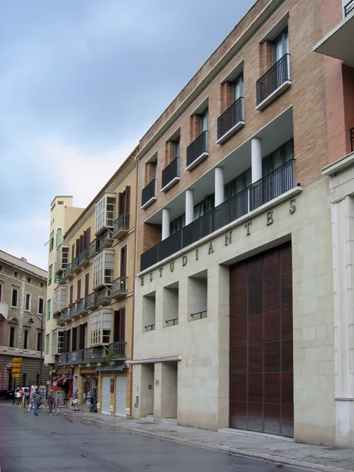 Vista exterior a pie de calle del edificio del Museo de la Cofradía de Estudiantes con la inscripción ESTUDIANTES en la fachada, una gran puerta de madera, balcones y peatones en la acera.